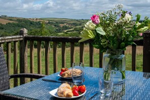 A table set outdoors with a view of rolling hills, a vase of flowers, and pastries with strawberries. - Bligh - cosy cottage near Crackington Haven (Cornwall)