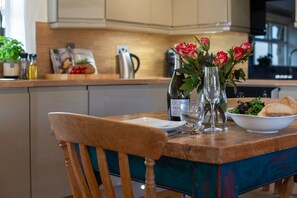 Une table à manger ornée d’un vase de fleurs, d’une bouteille de vin et d’un saladier.