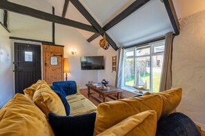 Un salon chaleureux avec un plafond en bois, un téléviseur et une vue sur l’extérieur.