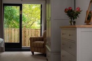 A room with a sliding glass door leading to a wooden deck, a striped armchair, a white dresser, and a vase with flowers.