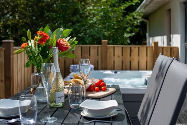 A dining table set with a bottle of Freixenet sparkling wine, a vase with red roses, a plate of bread, and a bowl of cherry tomatoes.
