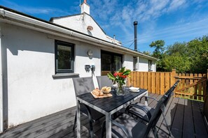 A patio with a table set for two, a chair, and a flower vase.