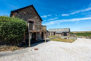 A stone building with a wooden balcony, gravel driveway, and a clear sky. - Butterwell - Treworgie Barton Cottages (Cornwall)