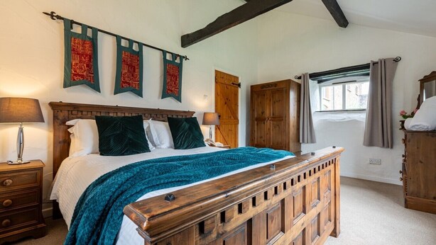 A bedroom with a wooden bed, a nightstand, a wardrobe, and a window with curtains. - Butterwell - Treworgie Barton Cottages (Cornwall)
