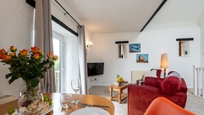 A modern living room with a red sofa, a dining table set for two, a TV, and artwork on the walls. - Butterwell - Treworgie Barton Cottages (Cornwall)