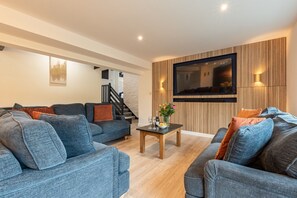 A modern living room with two sofas, a coffee table, and a flat-screen TV mounted on a wooden wall.