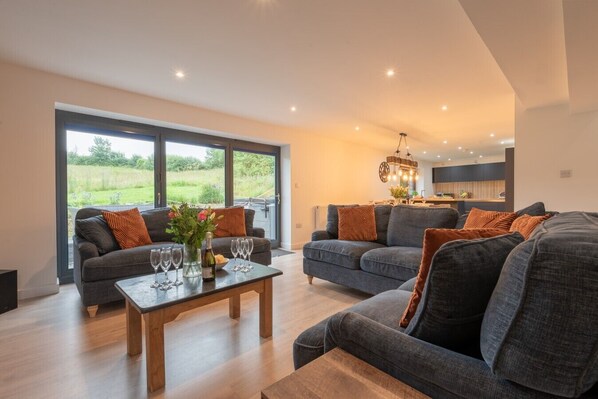 A modern living room with two sofas, a coffee table, and a dining area with a chandelier. - Manor a spacious modern cottage for families or groups (Cornwall)