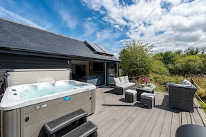 A hot tub on a wooden deck with outdoor furniture and a covered patio area. - Manor a spacious modern cottage for families or groups (Cornwall)