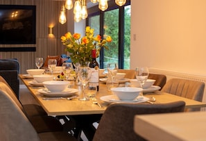 A dining table set with white dishes, glasses, and a bottle, with a vase of yellow flowers in the center.