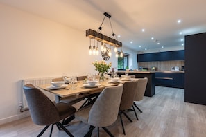 A modern kitchen with a central island, a dining area with a wooden table and chairs, and a pendant light fixture. - Manor a spacious modern cottage for families or groups (Cornwall)