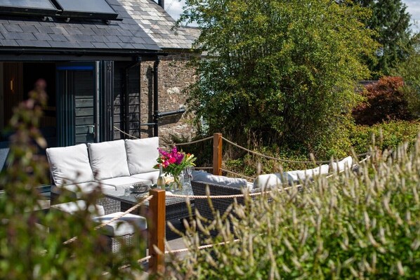 An outdoor seating area with a sofa and table, surrounded by greenery and a rope barrier.