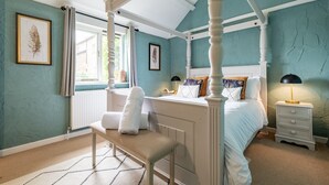 Un lit à baldaquin avec une literie blanche, une table de chevet avec une lampe et une fenêtre avec des rideaux.
