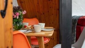 A dining area with a wooden table, orange chairs, and a vase of flowers. - Trespaddick - Treworgie Barton Cottages (Cornwall)