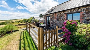 A stone building with a wooden deck, outdoor seating, and a view of the countryside. - Trespaddick - Treworgie Barton Cottages (Cornwall)