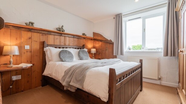 A bedroom with a wooden headboard, a single bed, a nightstand with a lamp, a window with curtains, and a radiator. - Trespaddick - Treworgie Barton Cottages (Cornwall)
