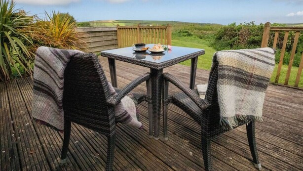 Een terras met rieten stoelen en een tafel, met uitzicht op een gazon.