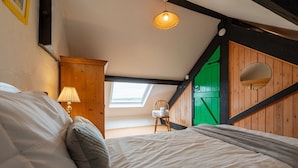 A bedroom with a bed, a chair, a lamp, a skylight, and a green door.
