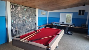 A pool table with cues in a room with blue walls and a chalkboard with drawings.