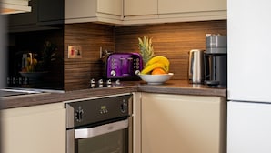 A kitchen with a built-in oven, a coffee maker, and a bowl of fruit on the counter.