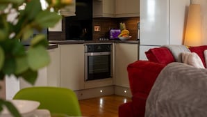 A modern kitchen with a built-in oven, a refrigerator, and a microwave. There is a dining area with a green chair and a red sofa.