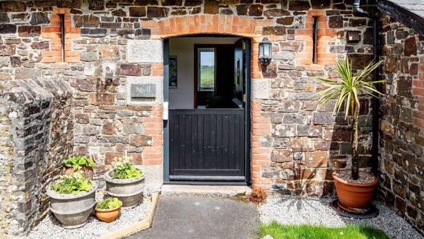 A stone building with a black door, potted plants, and a sign reading "Myl."