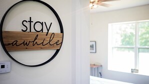 Eine runde Wanddekoration mit dem Schriftzug "stay awhile" und einem Thermostat an der Wand.