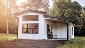 Ein zweistöckiges Haus mit großem Fenster, einer Veranda und einem Grill vor der Tür.