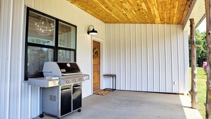 Ein überdachter Außenbereich mit Grill, großem Fenster und Holzboden.