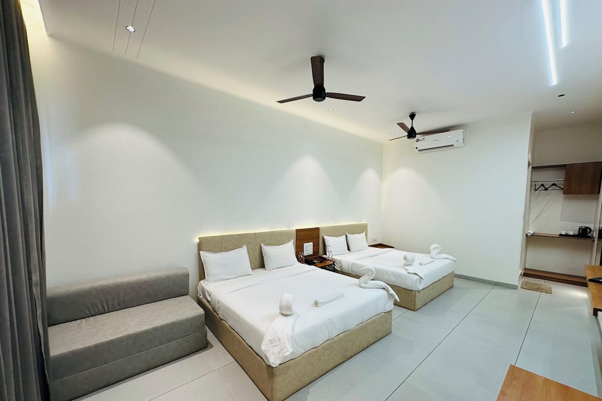 A hotel room with two beds, a sofa, a desk, and a ceiling fan.