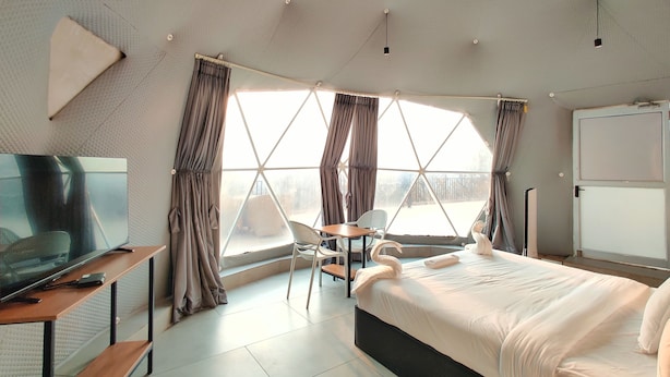 Una habitación de hotel moderna con un ventanal grande, una cama, un televisor y una zona de estar.