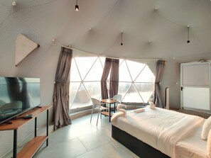 Una habitación de hotel moderna con un ventanal grande, una cama, un televisor y una zona de estar.