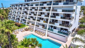 Um hotel com vários andares, varandas, piscina e palmeiras.
