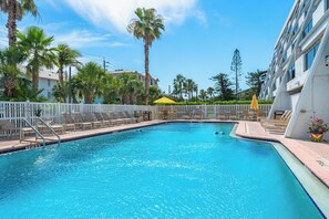 Relax by the pool surrounded by lush greenery and palm trees, with lounge chairs and umbrellas at your disposal.