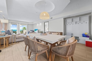 A spacious living room with a large dining table, wicker chairs, a ceiling light, and a view of the ocean.