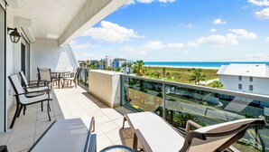 Ein Balkon mit Sitzmöbeln, freier Blick auf den Strand und ein modernes Gebäude im Hintergrund.