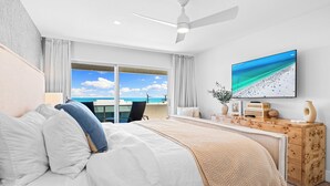 A modern hotel room with a large bed, a ceiling fan, a television, and a view of the beach through the window. - Tivoli by the Sea! Beach View Condo! Unit 504 (Siesta Key)