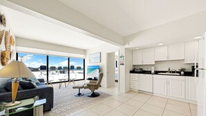 A modern living room with a sofa, armchair, and glass coffee table. A large window offers a view of the city skyline. - Tivoli by the Sea! Pool/Tennis/RecRoom! Unit 701 (Siesta Key)