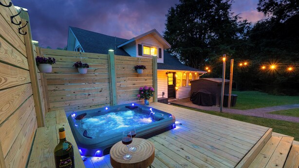Eine Holzterrasse mit Whirlpool, einer Weinflasche und zwei Gläsern auf einem kleinen runden Tisch.
