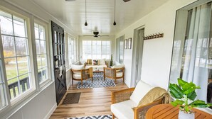 Ein geräumiges Zimmer mit großen Fenstern, einem Deckenventilator und einer Sitzecke mit Tisch und Stühlen.