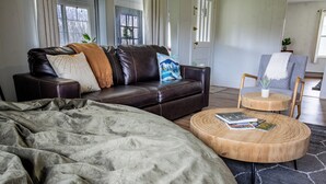 Ein modernes Wohnzimmer mit einem dunkelgrünen Ledersofa, einem runden Holztisch und einer flauschigen, grauen Decke.