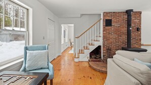 A cozy living room with a fireplace, a staircase, and a view of the outside. - Green Mountain Getaway (Waitsfield)