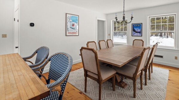 A dining room with a wooden table and chairs, a chandelier, and framed pictures on the walls. - Green Mountain Getaway (Waitsfield)