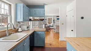A modern kitchen with blue cabinets, a wooden countertop, and a view into the living area. - Green Mountain Getaway (Waitsfield)