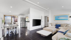 A modern living room with a flat-screen TV, a dining area with a table and chairs, and a kitchen with a refrigerator. - Spacial Rend in Cape Woolamai (Cape Woolamai)