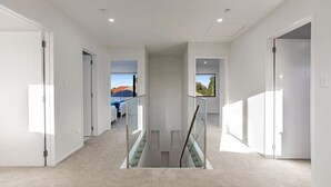 Un pasillo moderno con barandilla de vidrio, que conduce a un dormitorio con vistas al exterior.