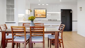 Una cocina moderna con armarios blancos, un refrigerador negro y un comedor con sillas de madera y una mesa de vidrio.
