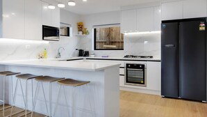 Una cocina moderna con armarios blancos, un refrigerador negro, horno empotrado y una zona de bar con taburetes.