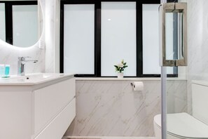 Un baño moderno con lavamanos, espejo, inodoro y ventana con paneles de vidrio esmerilado.