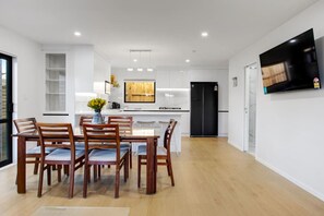 Una cocina moderna con armarios blancos, un refrigerador negro y un comedor con sillas de madera y una mesa.