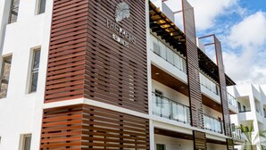 Un hotel de varios pisos con un diseño moderno, que presenta un logotipo destacado en la fachada y balcones en cada planta.
